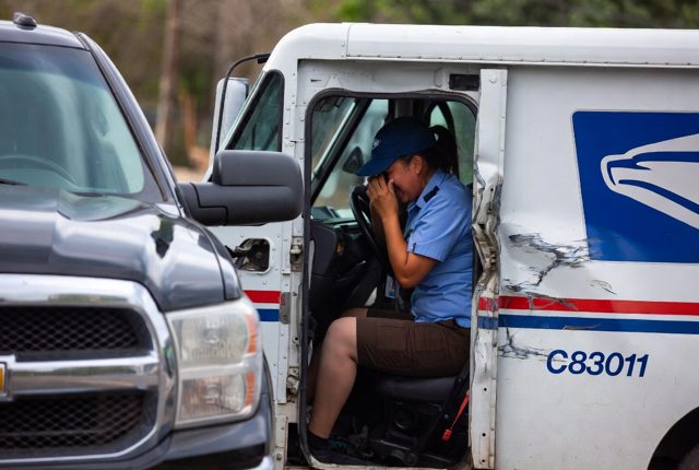 A USPS worker sits shaken in a damaged mail truck after a vehicle accident.